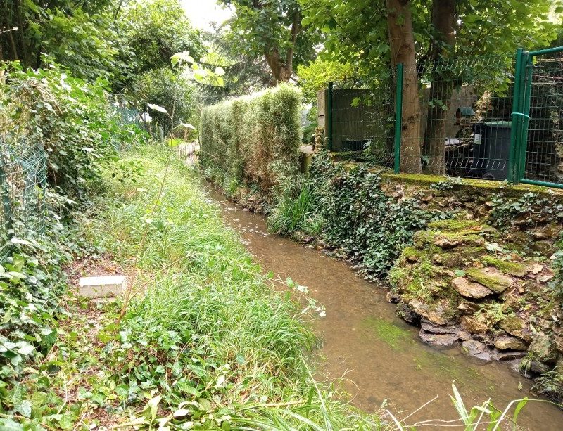 Un petit cours d'eau avec d'un côté un mur en pierre et un grillage